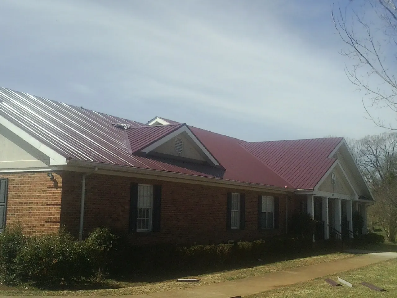 Red metal roof with gabled entries on a long brick building, from a Hail Damage Roof Repair job in Hampstead
