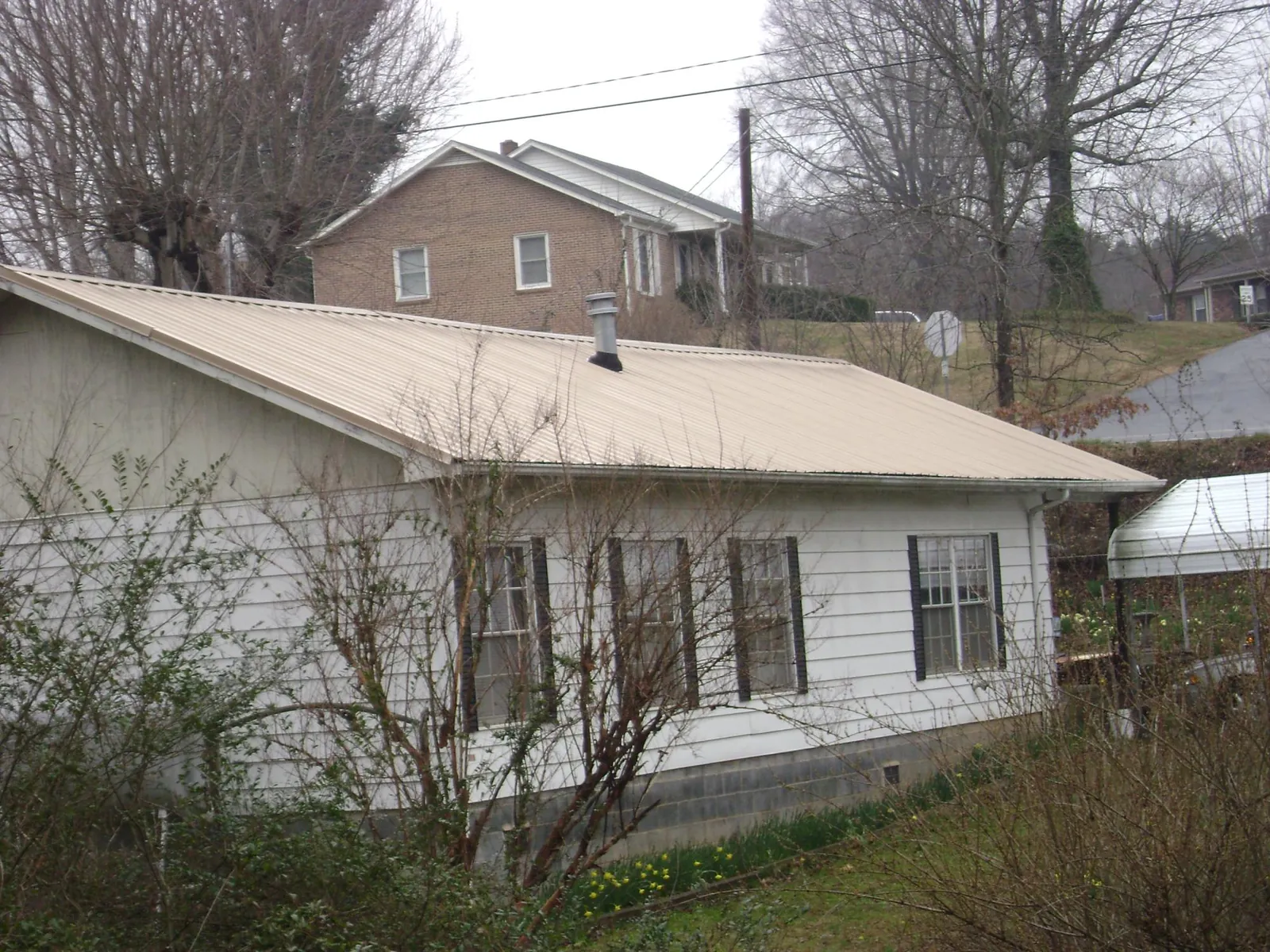 Tan metal roof on a white sided house set into a hillside — Commercial Roofing by Roofing Brothers in Hampstead